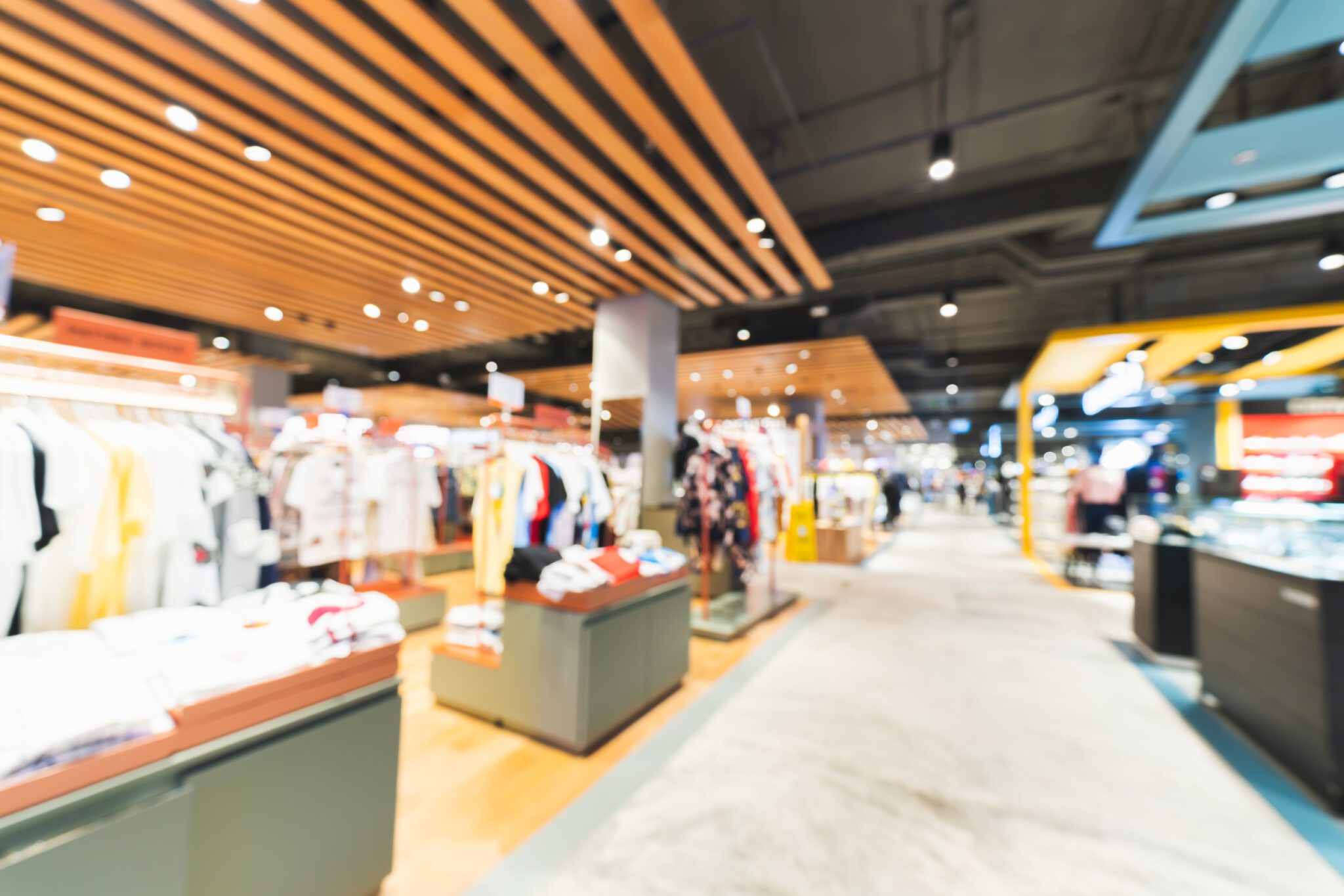 Blurred, defocused background of clothing shops in modern shopping mall or department store. Shopaholic lifestyle, or fashion dress outlet business concept