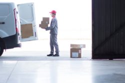 Courier worker delivering parcels and boxes in doorway of large warehouse