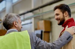 Happy factory worker communicating with company manager at woodworking industrial facility.