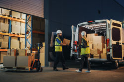 Outside of Logistics Retailer Warehouse With Female Manager Using Tablet Computer, Worker Loading Delivery Truck with Cardboard Boxes. Online Orders, Purchases, E-Commerce Goods, Supply.