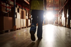 Professional Warehouse Worker Wearing Safety West Walking Through The Strorage Facility, Distribution, Delivery Center. Emotional, Moody Back View Silhouette Shot