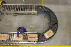 Elevated view of female worker scanning boxes on a conveyor belt in a warehouse