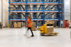Defocused shot of a woman worker moving boxes in a warehouse using a hand truck. Motion blur of an employee using a pallet truck to move stock in a storehouse.