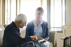 Nurse discussing with senior man over medicine. Confident female caregiver is explaining elderly man. They are sitting at home.