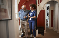 Mature female nurse walking with senior man on steps at home