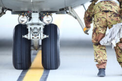 An army mechanic is inspecting the landing gear of a military cargo plane.