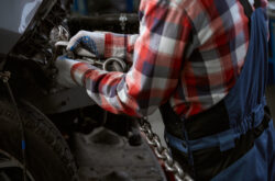 Worker in a car repair shop attaches a carabiner with a chain to the car body